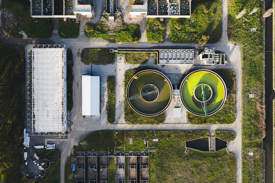 Aerial view of circular pools reflecting the sky amid industrial structures and green spaces, creating a striking contrast, Rome, Lazio, Italy.