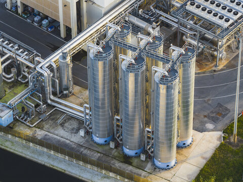Aerial view of industrial tanks gleaming under the sunlight, interconnected by a network of pipes, casting shadows on the concrete below, Rome, Lazio, Italy.