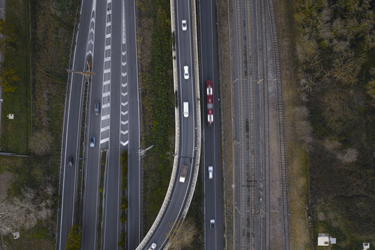 Aerial view of a highway curving alongside a train track, the vehicles casting small shadows on the asphalt, Rome, Lazio, Italy.