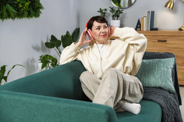 Obraz premium Woman with headphones listening music on sofa at home. Space for text