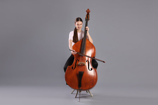 Girl playing double bass on grey background