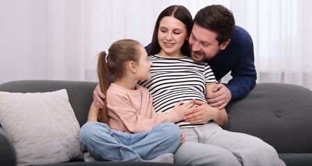 Obraz premium Pregnant woman, her husband and daughter on sofa at home