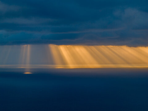 Aerial view of radiant golden rays piercing through the dark, brooding clouds, illuminating the tranquil sea below, Tias, Lanzarote, Canary Islands.