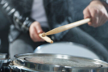 Obraz premium Man with drumsticks playing drum in smoke on black background, closeup