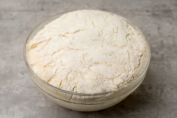 Fresh yeast dough in glass bowl on gray textured table, closeup