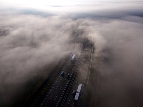 Aerial view of vehicles navigating through a sea of fog along a highway, Rivoli, Piedmont, Italy.