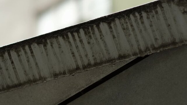 Close up of water droplets sliding down a metal ledge and dripping into the air