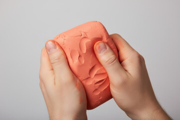 Hands squeezing soft pink kinetic sand block with fingerprints. Closeup studio shot for sensory play concepts, stress relief therapy and children creative activities