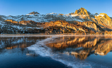 Obraz premium Sunset over the Alps mountain with reflection on the frozen lake with curvy opaque ice line on the Silsersee Lake in St. Moritz, Grisons, Switzerland