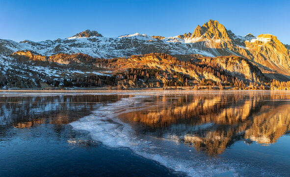 Sunset over the Alps mountain with reflection on the frozen lake with curvy opaque ice line on the Silsersee Lake in St. Moritz, Grisons, Switzerland