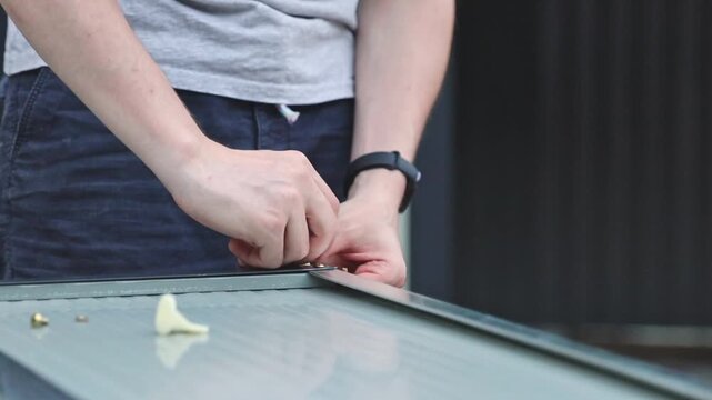 An unrecognizable handyman manually installs corner brackets on a metal barn door.