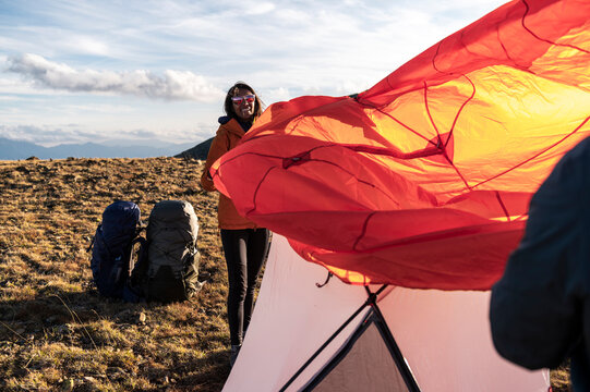Smiling hiker holding glowing tent rainfly in mountain wind