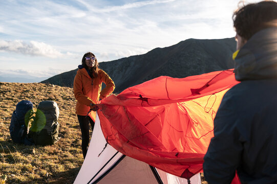 Friends coordinating tent setup against shifting mountain wind