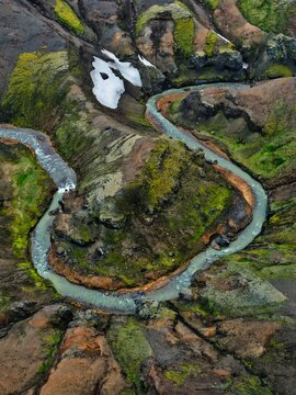 Aerial view of a vibrant river snaking through a valley of mossy greens, earthy browns, and patches of snow, central highlands, Hrunamannahreppur, Iceland.