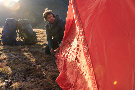 Focused male hiker fastening tent fabric in golden light