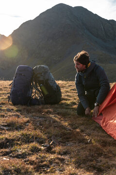 Focused hiker securing tent anchor during windy mountain dusk