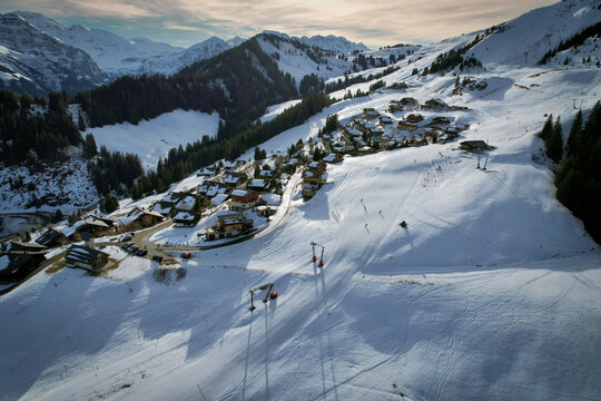 Aerial view of snow-blanketed chalets nestling amidst jagged peaks, a winter wonderland of contrasting whites and dark greens, Val-d'Illiez, Valais, Switzerland.