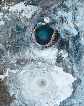 Aerial view of the Strokkur geyser and other hot springs surrounded by mineral deposits with a person standing in the landscape, Geysir, Blaskogabyggd, Iceland.