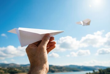 A person's hand holds a paper airplane, ready to launch it into a bright blue sky, symbolizing freedom, travel, and imagination.