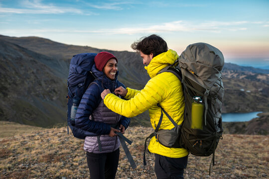 Smiling hikers adjusting gear while sharing moment in mountains