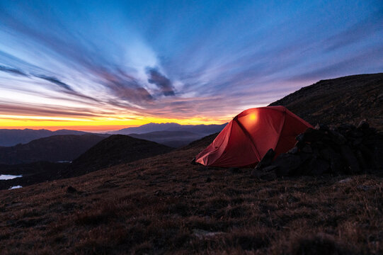 Illuminated tent facing dramatic sunset above vast mountain range