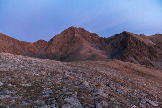 Tiny tent dwarfed by expansive mountain terrain in fading light