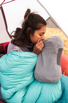 Female hiker inflating inflatable pillow sitting in sleeping bag inside tent