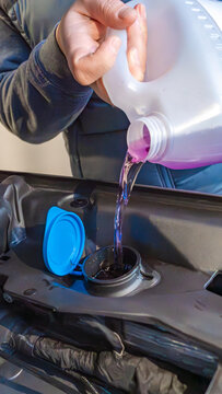 Person pouring purple liquid into a car's reservoir cap, showcasing automotive maintenance in a close-up view of the engine compartment