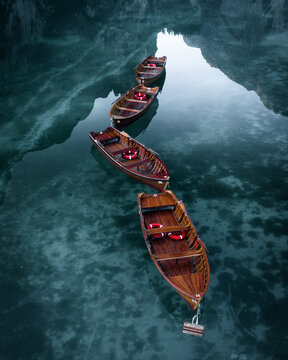 Aerial view of wooden boats float on the crystal clear waters of Lago Di Braies, Italy.