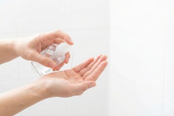 Naklejka premium A person dispensing clear hand sanitizer from a spray bottle into their palm for hygiene.