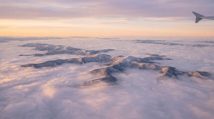 Aerial view of snow-capped mountains emerging from a sea of clouds at sunrise