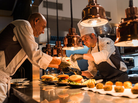 Chefs preparing gourmet cheeseburgers in kitchen