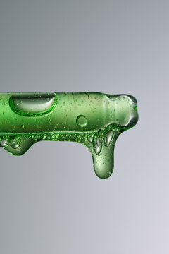 Close-up of green serum with bubbles dripping down on a gray backdrop.