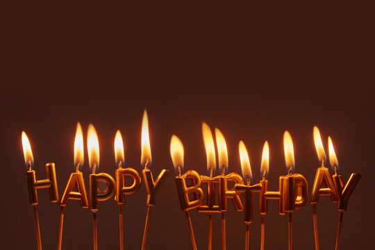 Gold happy birthday letter candles on dark background