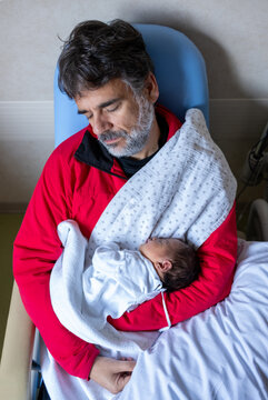 Man Sleeping In Hospital Chair Holding Newborn Baby