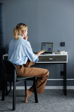 Back view of company CEO watching digital app on laptop on nightstand