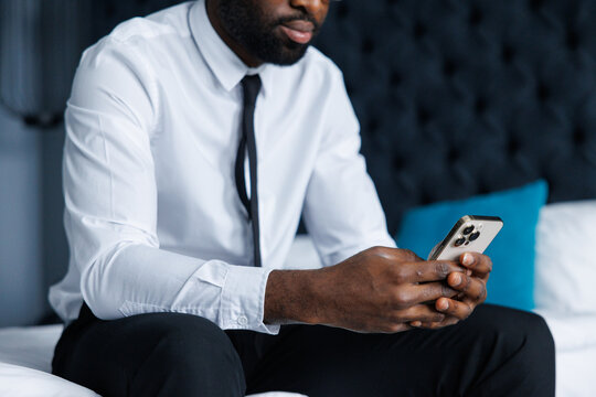 Obscure face of black businessman using cellphone sitting on bed