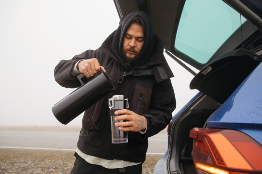 man doing coffee using thermos in cold day near car