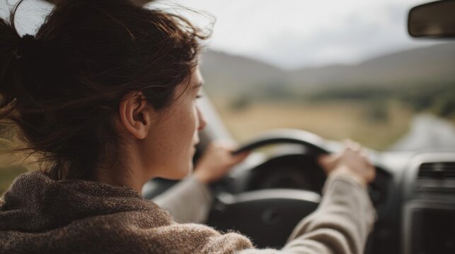 Young woman driving a car on a road. she is holding the steering wheel with both hands and appears to be focused on the road ahead.
