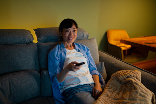 Asian woman relaxing watching tv using remote control
