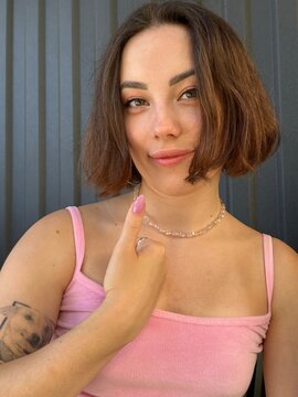 A cute brunette girl with a bob haircut and a tattoo in a pink T-shirt