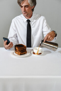 Businessman pouring coffee while distracted by phone and burnt toast