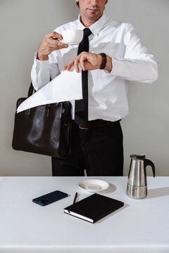 Man in formal attire holding coffee and documents while checking time