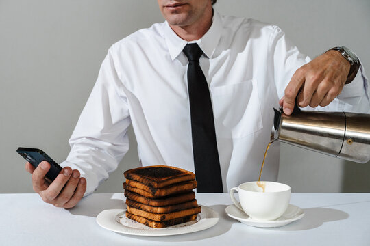 Man pouring coffee, spilling it past cup while looking at phone screen