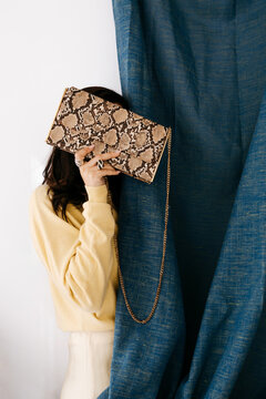 Woman hiding face behind snakeskin clutch bag