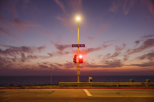 Traffic light and streetlamp by ocean at sunset