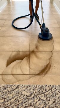 Professional cleaner using a rotary scrubber machine on dirty beige tile flooring to remove dark grime from grout lines, illustrating deep cleaning and restoration services.