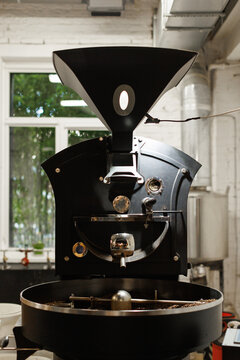 Front view of coffee roaster with coffee beans during work in workshop