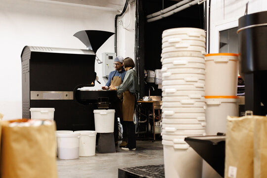 Woman looking at coworker checking degree of roast in roaster machine