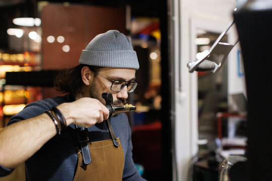 Young focused male worker sniffing coffee beans before roasting